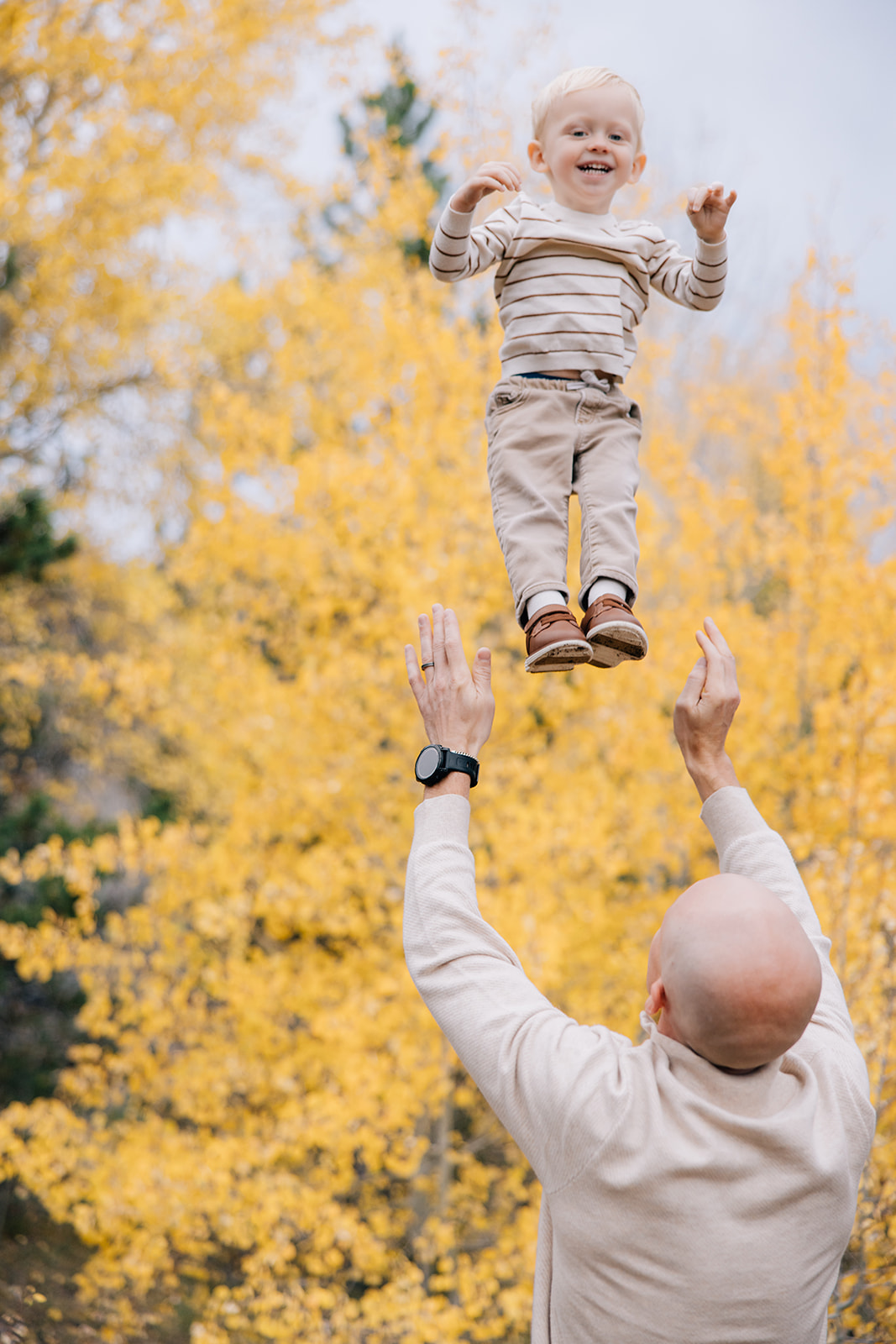 A toddler in tan is tossed up high by dad during one of the fall activities in Breckenridge, Colorado