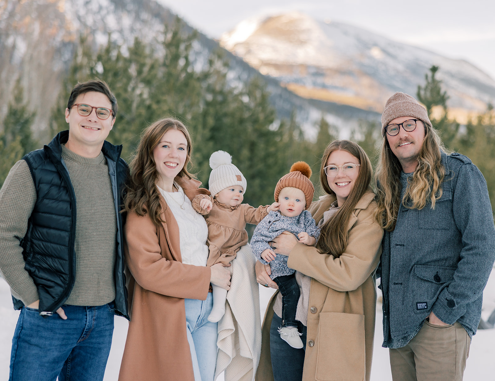 Two sets of happy parents smile while holding their two baby girls in a snow covered mountain pass during one of the Breckenridge ski resort activities