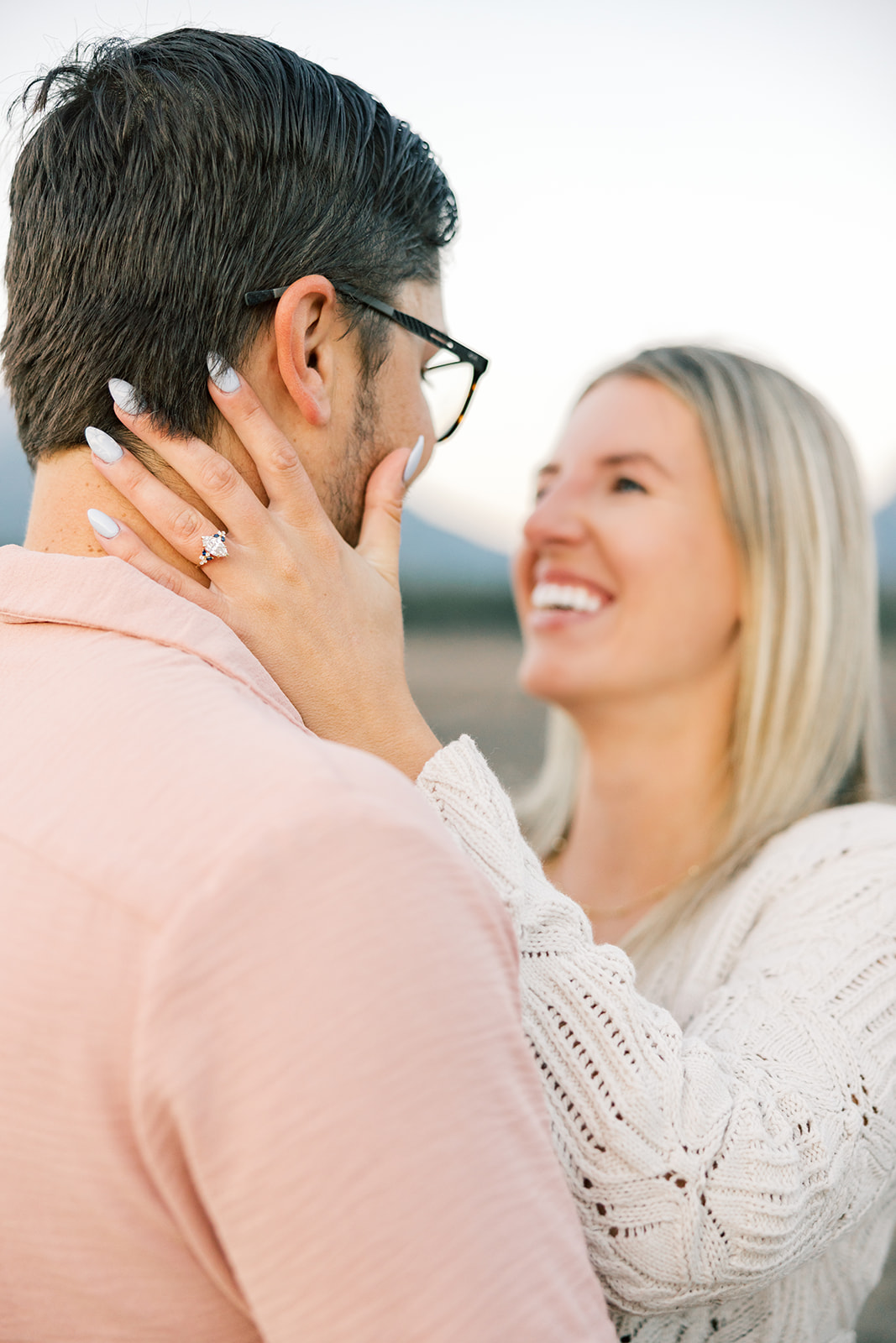 Details of a woman's ring hand with new engagement ring on her fiancee's neck as they hug and laugh at one of the places to propose in Breckenridge
