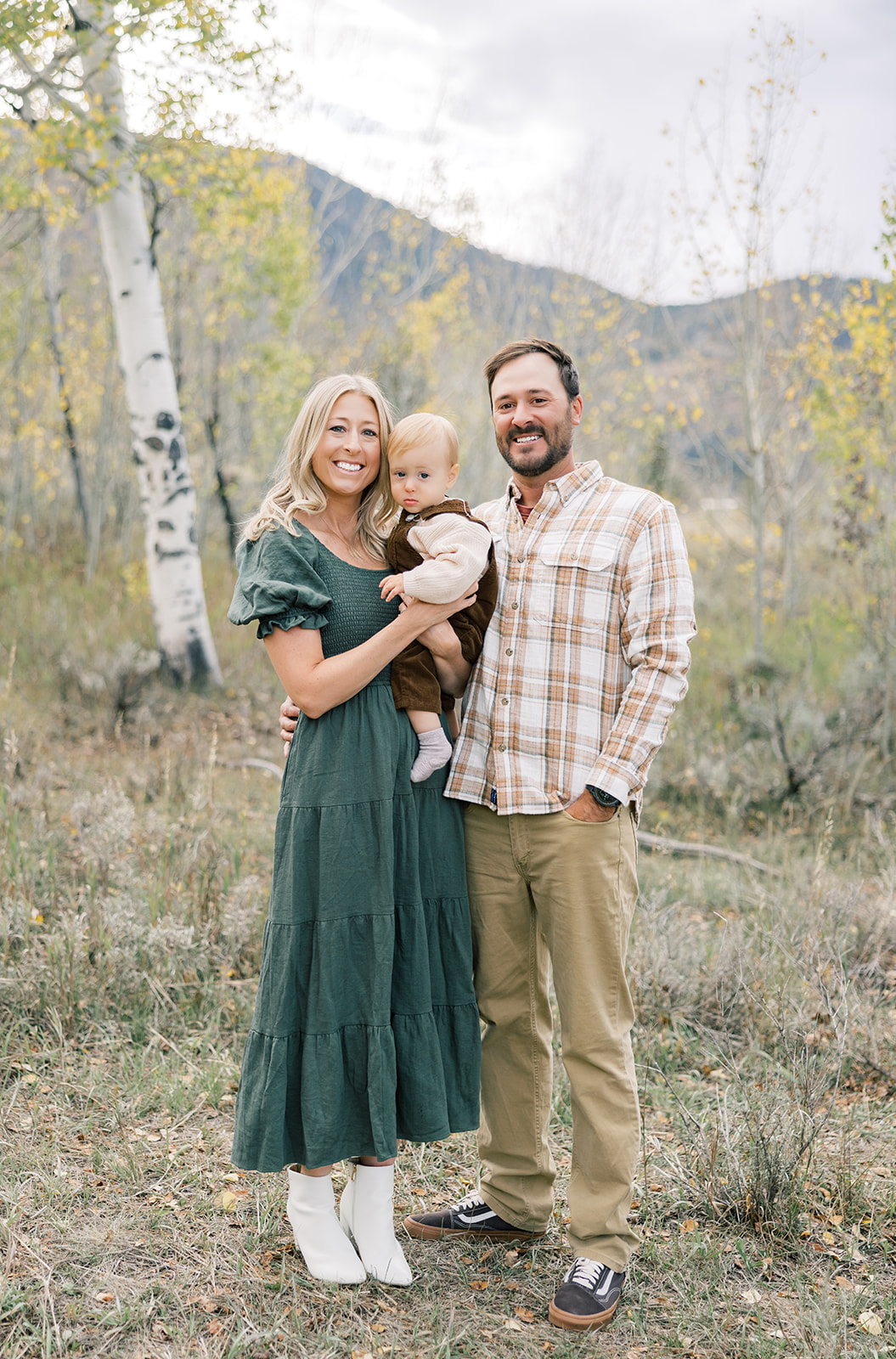 Happy parents hold their toddler son in a forest in fall