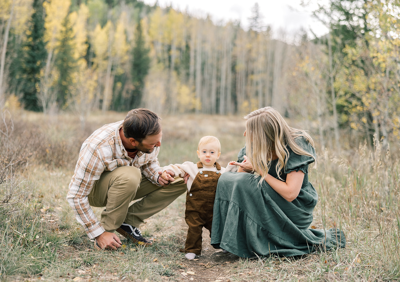 A mom and dad help their toddler son walk in a forest trail in fall while enjoying long term rentals in Breckenridge, CO